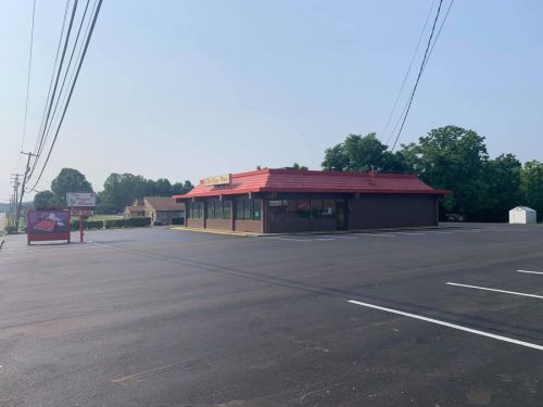 A fast-food restaurant with a red roof, surrounded by a freshly paved parking lot and trees in the background.