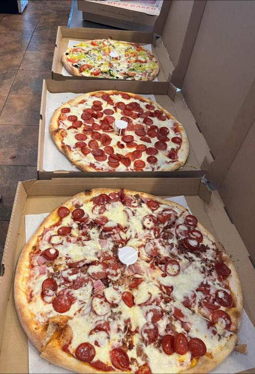Three large pizzas in cardboard boxes: one with pepperoni, one with mixed toppings, and one with pepperoni and ham.