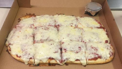 A rectangular pizza with melted cheese and tomato sauce, cut into square slices, in a cardboard box.