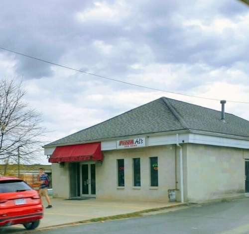 A pizza restaurant named "Al's" with a red awning, a parked red car, and a person walking by under a cloudy sky.