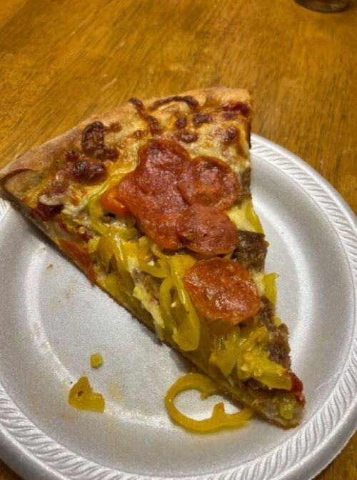 A slice of pizza on a paper plate, topped with pepperoni, yellow peppers, and melted cheese.