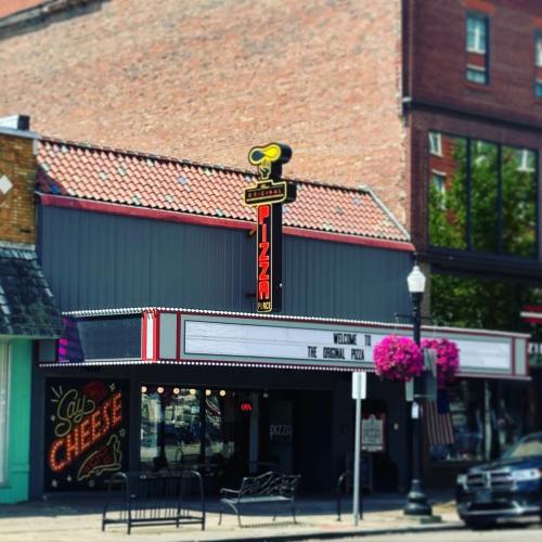 A vintage pizza restaurant with a neon sign, colorful flowers, and a welcoming marquee in a downtown setting.