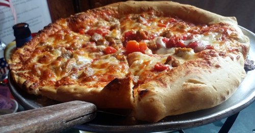 A freshly baked pizza with melted cheese, toppings of sausage, tomatoes, and a golden crust on a serving tray.