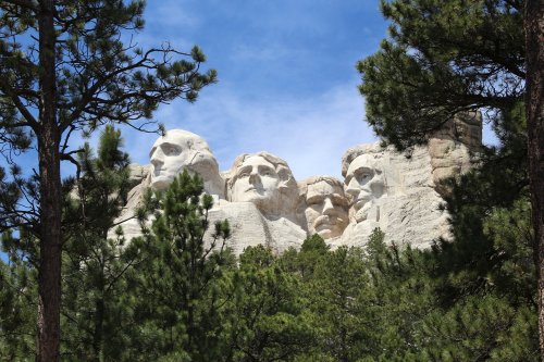 Mount Rushmore monument partially obscured by trees, featuring the carved faces of four U.S. presidents against a blue sky.
