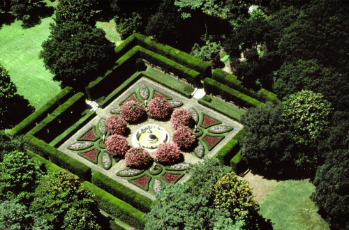 Aerial view of a beautifully landscaped garden with a central fountain surrounded by colorful flower beds and hedges.