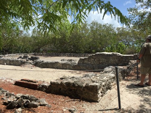 Ruins of an ancient structure surrounded by greenery, with a person observing the site in the background.