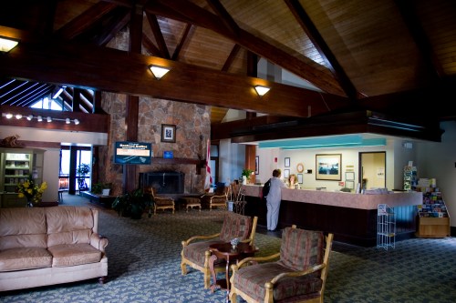 A spacious lobby with wooden beams, a stone fireplace, and a reception desk, featuring comfortable seating areas.