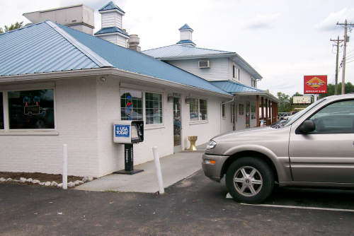 A white building with a blue roof, featuring a sign and a parked car in front.