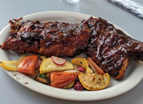 A plate of grilled ribs glazed with barbecue sauce, served with a side of roasted vegetables and potatoes.