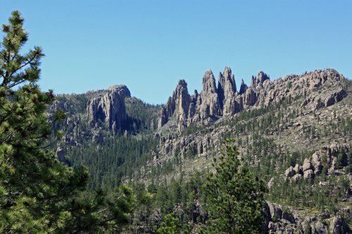 A scenic view of rugged mountain peaks surrounded by lush green forests under a clear blue sky.