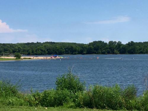 A serene lake scene with a sandy beach, people enjoying the water, and lush greenery in the foreground.