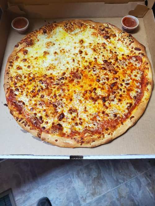 A large cheese pizza in a cardboard box, with two small cups of marinara sauce on the side.