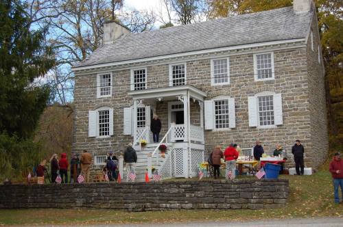 A historic stone house with people gathered outside, some with flags, during a community event in autumn.