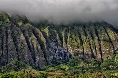Lush green mountains with steep ridges, partially shrouded in clouds, creating a dramatic landscape.