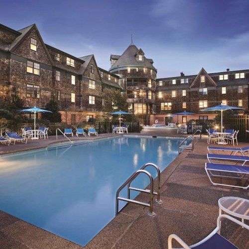 A serene hotel pool area at dusk, surrounded by lounge chairs and a charming building in the background.