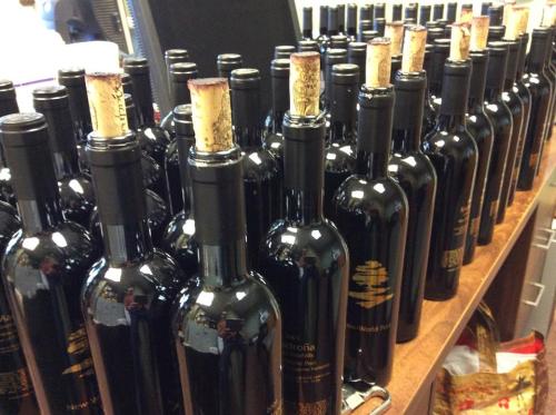 A row of dark wine bottles with corks, lined up on a wooden surface in a storage area.