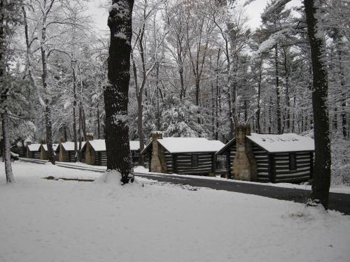 Snow-covered log cabins nestled among trees in a winter landscape, with a clear path leading through the snow.