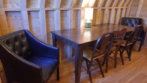 A wooden table surrounded by chairs and two black armchairs in a cozy, wooden-paneled room.