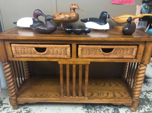 A wooden table with two woven drawers, topped with various decorative duck figurines.