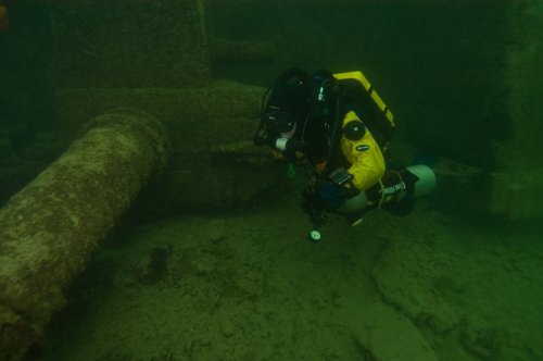 A diver explores an underwater site, surrounded by murky water and submerged structures.