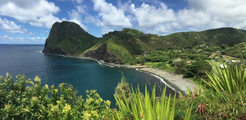 A panoramic view of a lush green coastline with rocky cliffs and a calm blue sea under a partly cloudy sky.