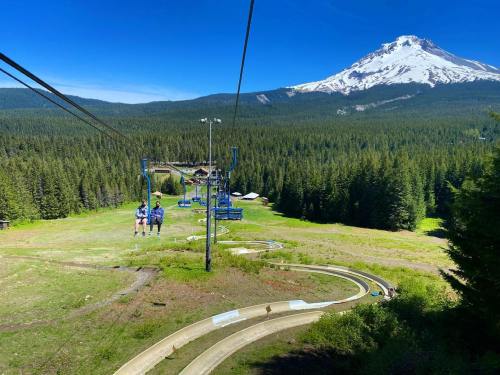Two people ride a chairlift over a green landscape with a mountain in the background on a sunny day.