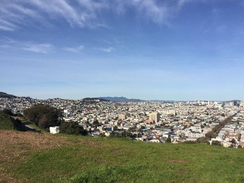 A panoramic view of a cityscape with buildings, hills, and a clear blue sky in the background.
