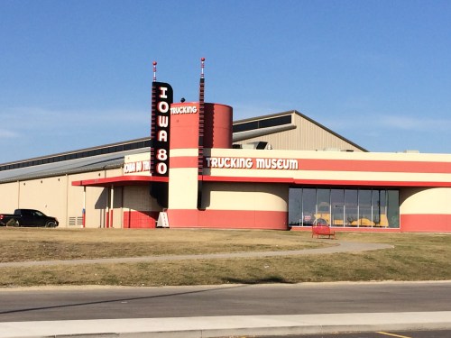 Exterior of the Iowa 80 Trucking Museum, featuring a red and cream building with a tall sign against a clear blue sky.