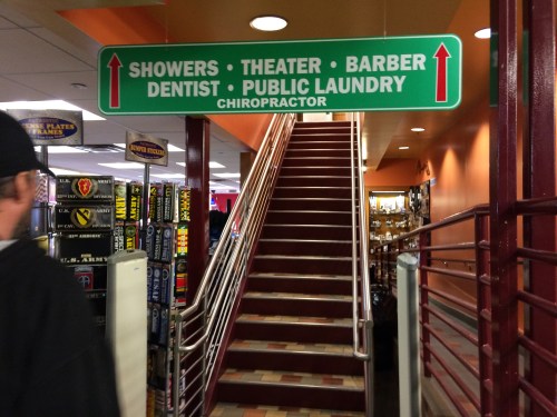 Sign directing to various facilities: showers, theater, barber, dentist, public laundry, and chiropractor, with stairs visible.