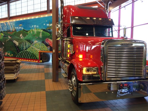 A bright red truck parked inside a building, with a colorful mural of rolling hills and fields in the background.
