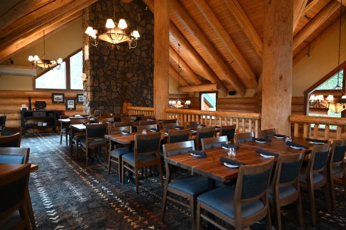 Cozy restaurant interior with wooden beams, stone fireplace, and neatly arranged tables. Warm, inviting atmosphere.