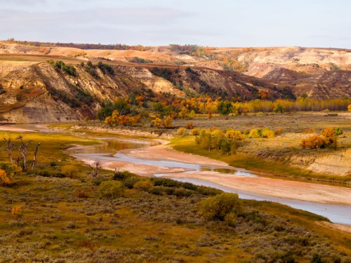 A scenic landscape featuring a winding river, colorful autumn foliage, and rugged hills under a clear sky.