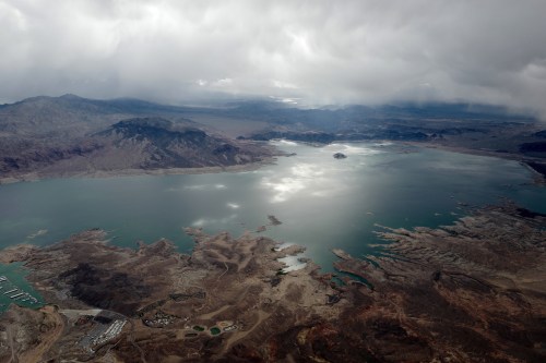 Aerial view of a vast lake surrounded by rugged terrain and mountains under a cloudy sky.