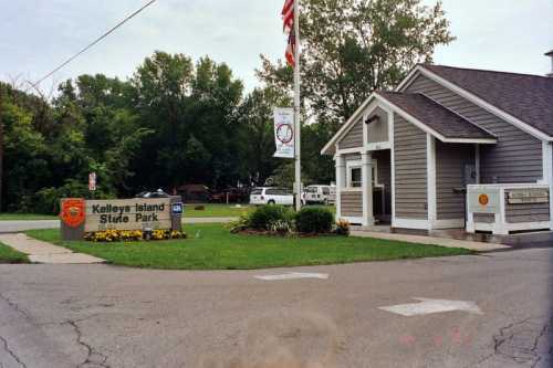 Entrance to Kelleys Island State Park, featuring a sign, flag, and park office surrounded by greenery.