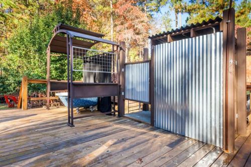 A wooden deck featuring a covered seating area and a corrugated metal enclosure surrounded by trees.