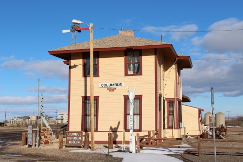 A two-story yellow building with red trim, labeled "Columbus Historical Museum," set against a blue sky.