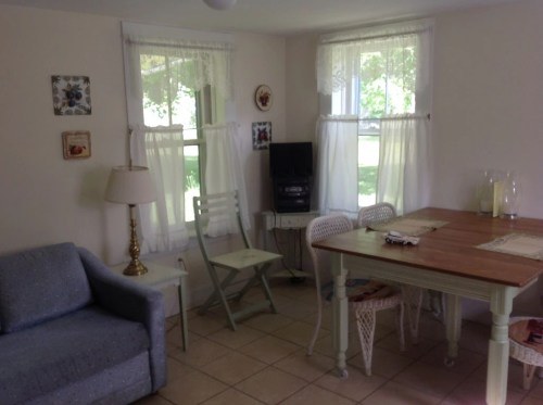Cozy room with a blue sofa, wooden table, chairs, and large windows with white curtains.