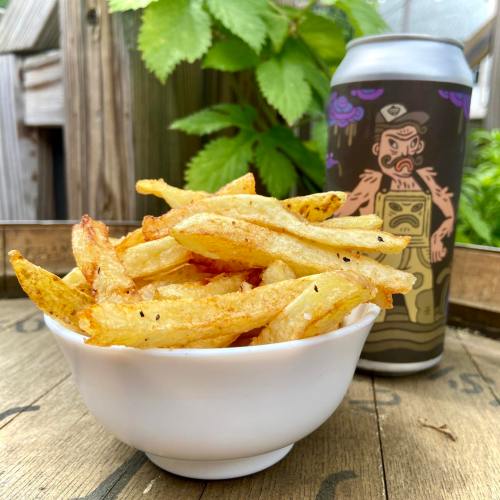 A bowl of golden fries next to a can of beer, set against a green, leafy background.