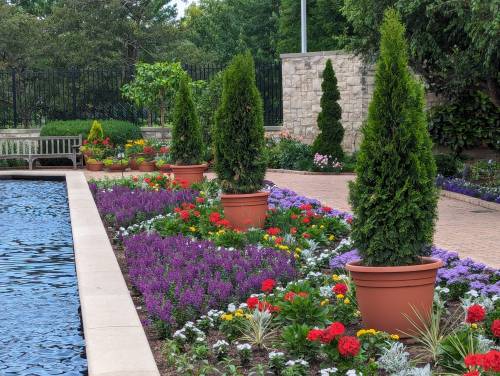 A landscaped garden featuring colorful flowers, neatly trimmed shrubs in pots, and a tranquil water feature.
