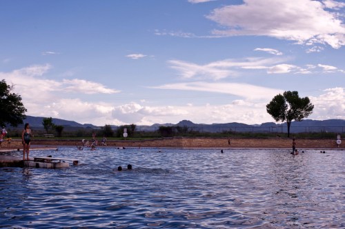 A serene swimming area with people enjoying the water, surrounded by mountains and a cloudy sky.
