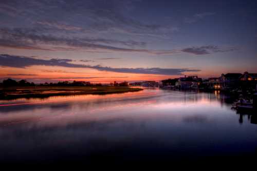 Serene sunset over a calm waterway, reflecting vibrant colors and surrounded by lush greenery and homes.