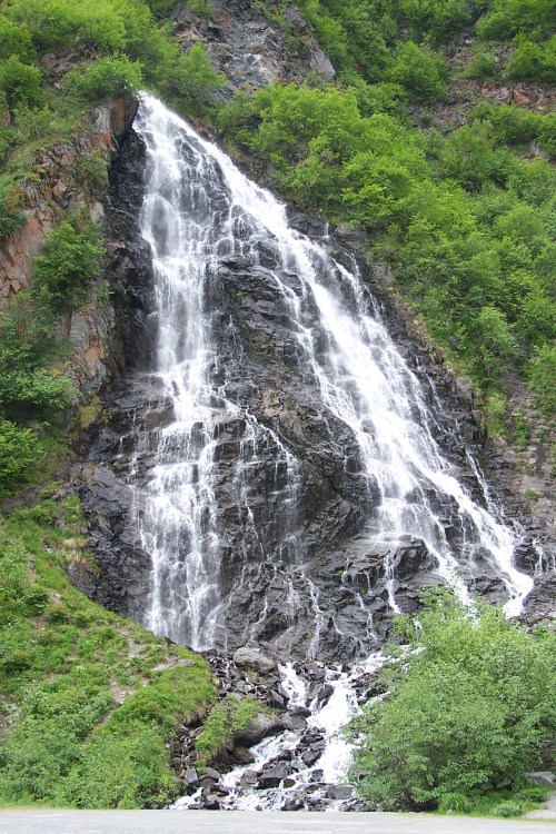 A cascading waterfall flows down rocky cliffs, surrounded by lush green vegetation.