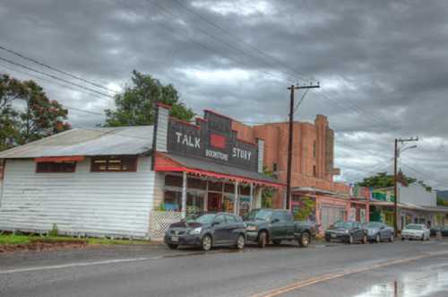 A quaint bookstore named "Talk Story" beside a street lined with parked cars and a cloudy sky overhead.