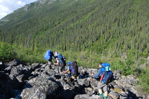 Hikers navigate rocky terrain in a lush, green mountainous landscape.