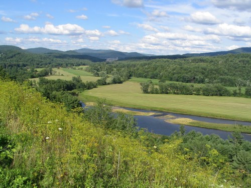 A scenic view of rolling green hills, a winding river, and a blue sky with fluffy clouds.