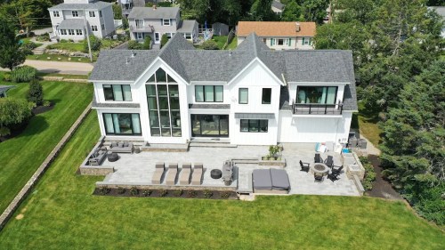 Aerial view of a modern white house with large windows, a patio, and landscaped yard.