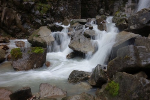 A serene waterfall cascading over large rocks, surrounded by moss and natural greenery.