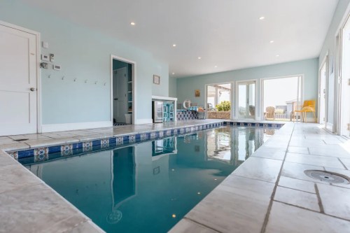 Indoor swimming pool with light blue walls, large windows, and a tiled border, featuring a bright, airy atmosphere.