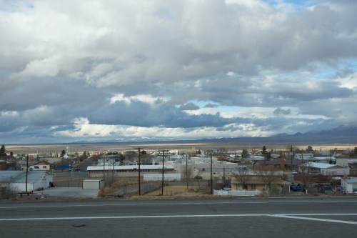 A view of a small town with scattered houses under a cloudy sky and distant mountains.