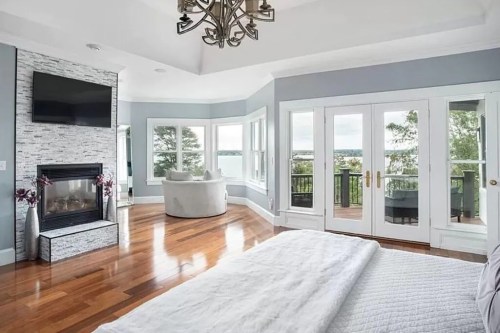 Bright, modern bedroom with a fireplace, large windows, and a view of the outdoors. Elegant decor and hardwood floors.